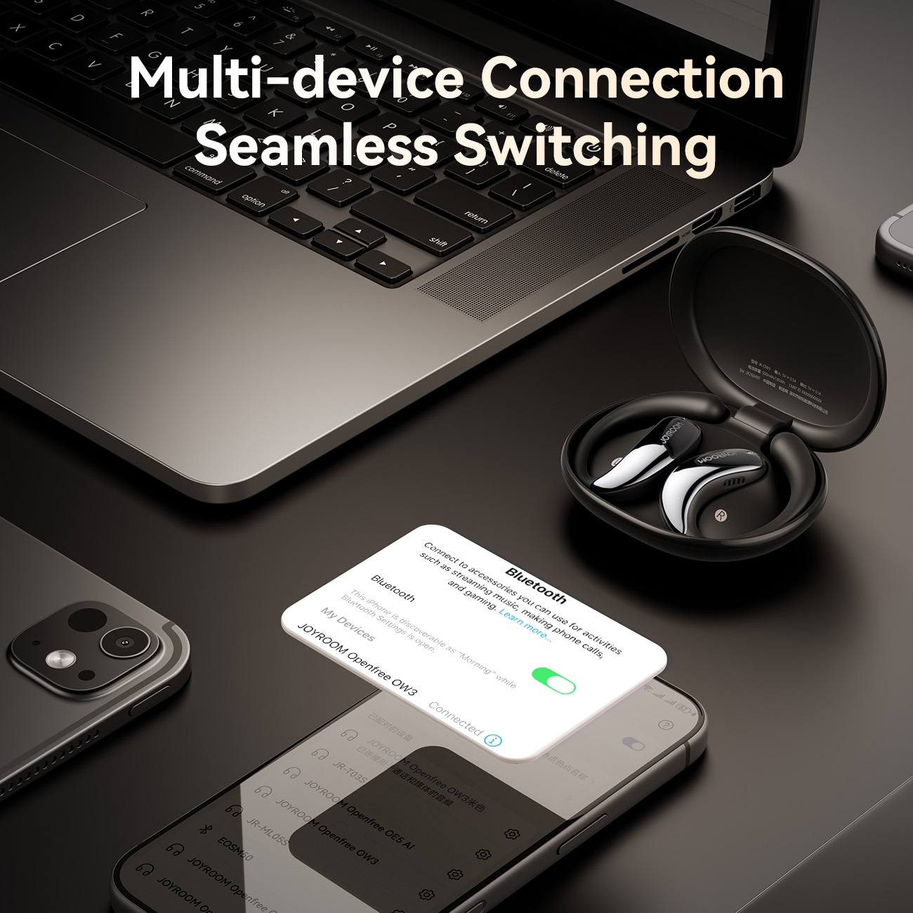 JOYROOM OW3 open-ear wireless earbuds on office desk illustrating dual multi-device Bluetooth connection and seamless switching between laptop and smartphone.