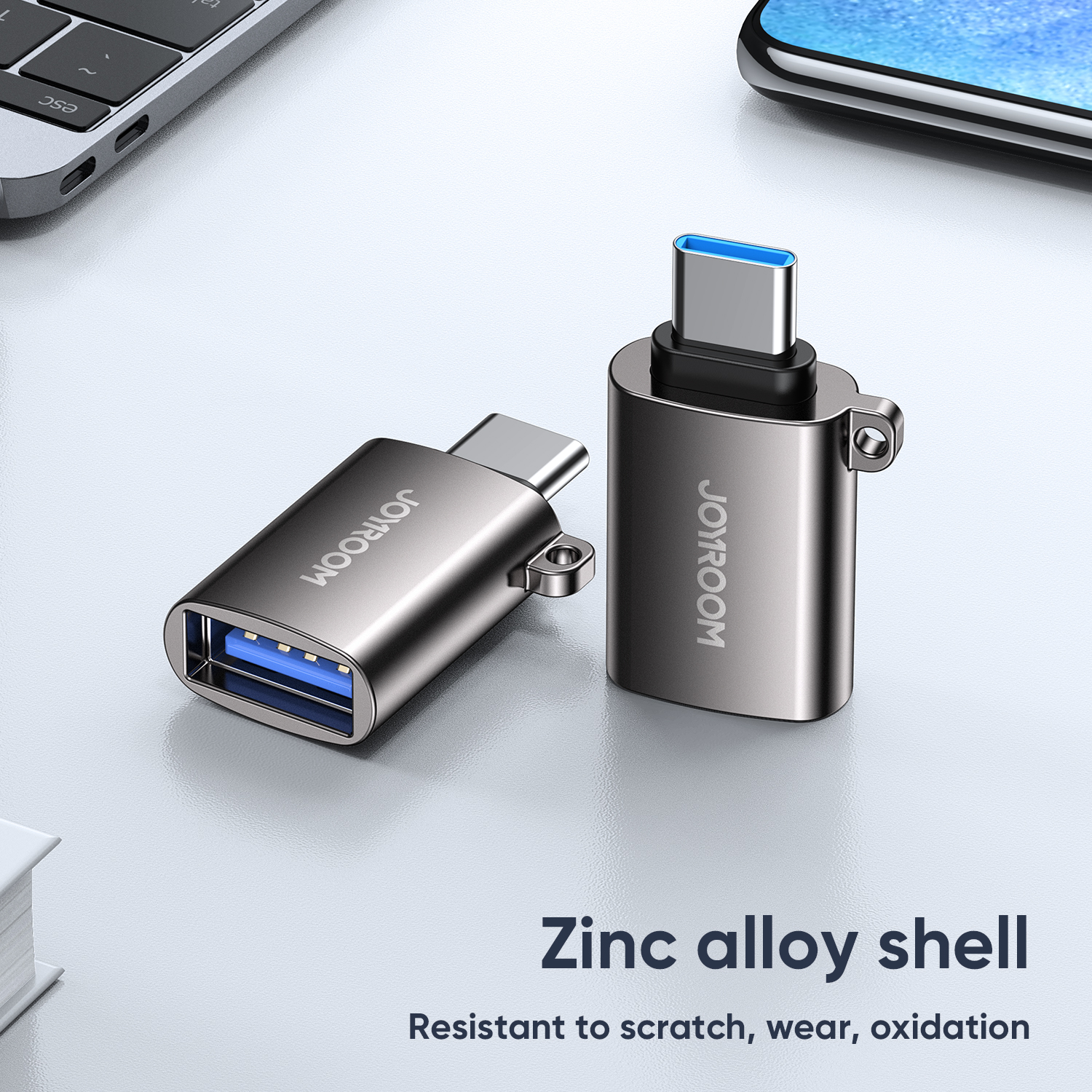 Two JOYROOM S-H151 Type-C Male to USB Female Adapters with a pearl nickel zinc alloy shell on a desk. The text reads 'Zinc alloy shell Resistant to scratch, wear, oxidation'. The image shows one adapter's blue USB 3.0 port and the other's Type-C connector, with a keyring loop visible.